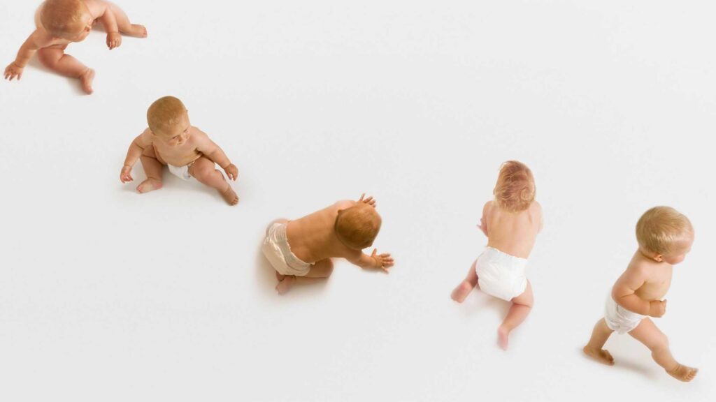 Imagem de fundo branco. Um bebê de cabelos loiros posa em diversas posições: sentado, agachado, engatinhando e andando. 