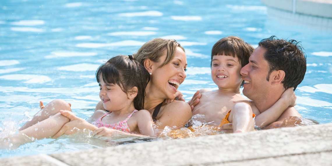 Pais brincando com os filhos em borda de uma piscina